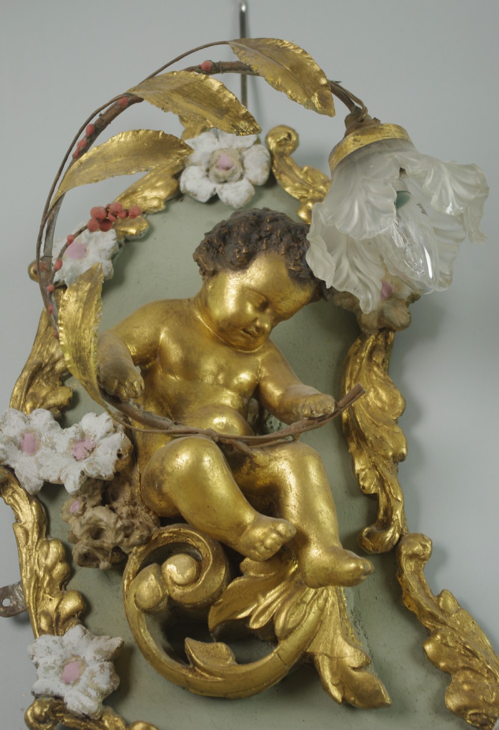 A pair of 19th-century French gilt wall lights featuring sculpted putti figures seated within asymmetrical gilded Rococo floral frames with frosted glass flower shades. View VI