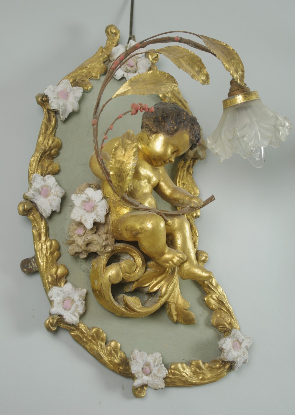 A pair of 19th-century French gilt wall lights featuring sculpted putti figures seated within asymmetrical gilded Rococo floral frames with frosted glass flower shades. View X