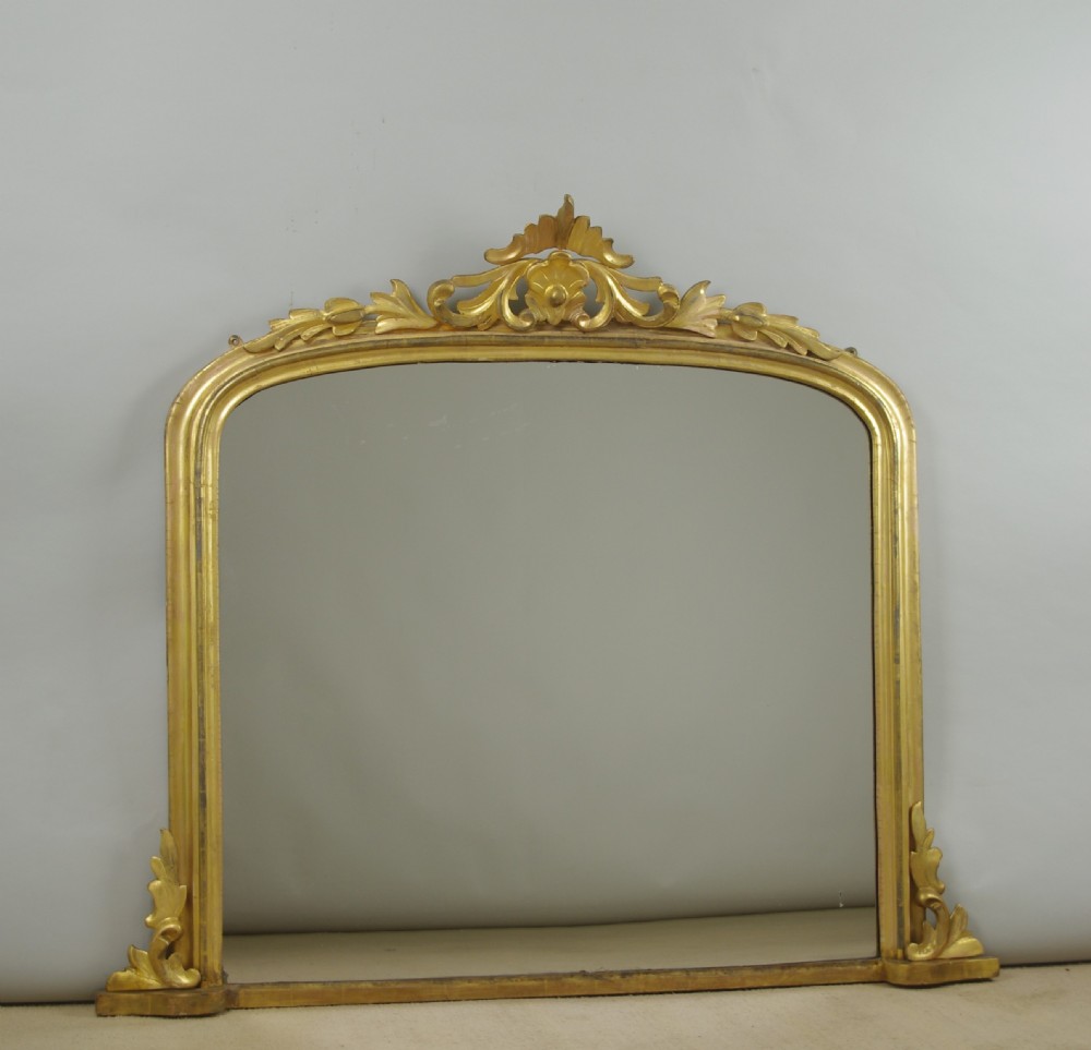 A Victorian giltwood overmantle mirror featuring an arched top frame, carved foliate cresting, and a flat base.