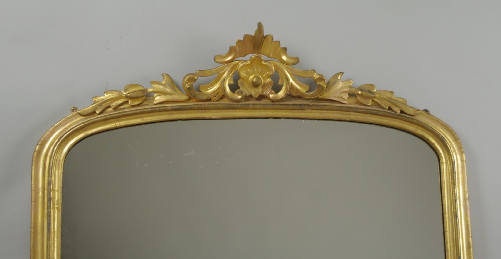A Victorian giltwood overmantle mirror featuring an arched top frame, carved foliate cresting, and a flat base. View II