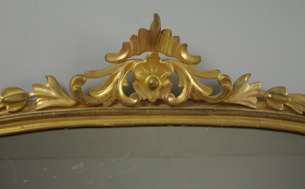 A Victorian giltwood overmantle mirror featuring an arched top frame, carved foliate cresting, and a flat base. View III