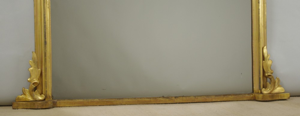 A Victorian giltwood overmantle mirror featuring an arched top frame, carved foliate cresting, and a flat base. View VIII