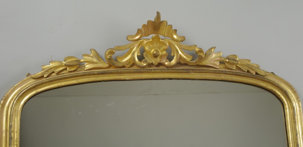 A Victorian giltwood overmantle mirror featuring an arched top frame, carved foliate cresting, and a flat base. View IX
