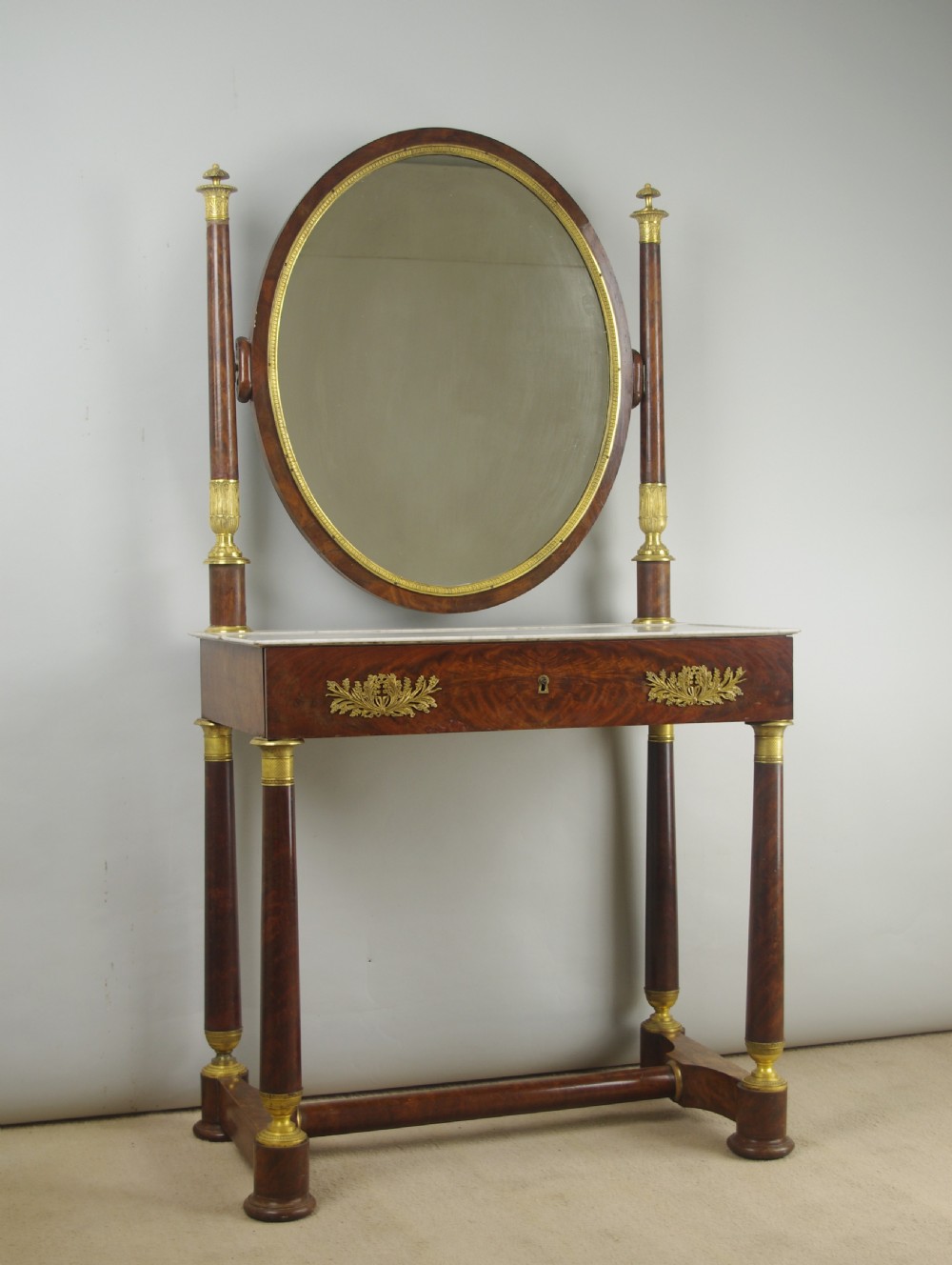 A French Empire mahogany dressing table featuring an oval swivel mirror flanked by gilt-bronze capped columns, set above a marble surface and drawer base with ormolu appliques. View II