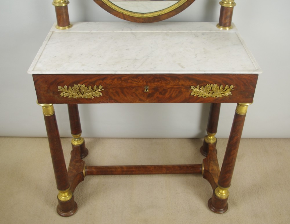 A French Empire mahogany dressing table featuring an oval swivel mirror flanked by gilt-bronze capped columns, set above a marble surface and drawer base with ormolu appliques. View VI
