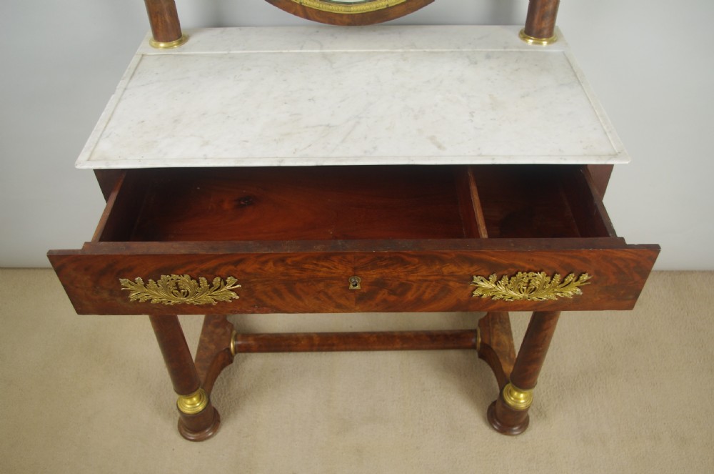 A French Empire mahogany dressing table featuring an oval swivel mirror flanked by gilt-bronze capped columns, set above a marble surface and drawer base with ormolu appliques. View VII