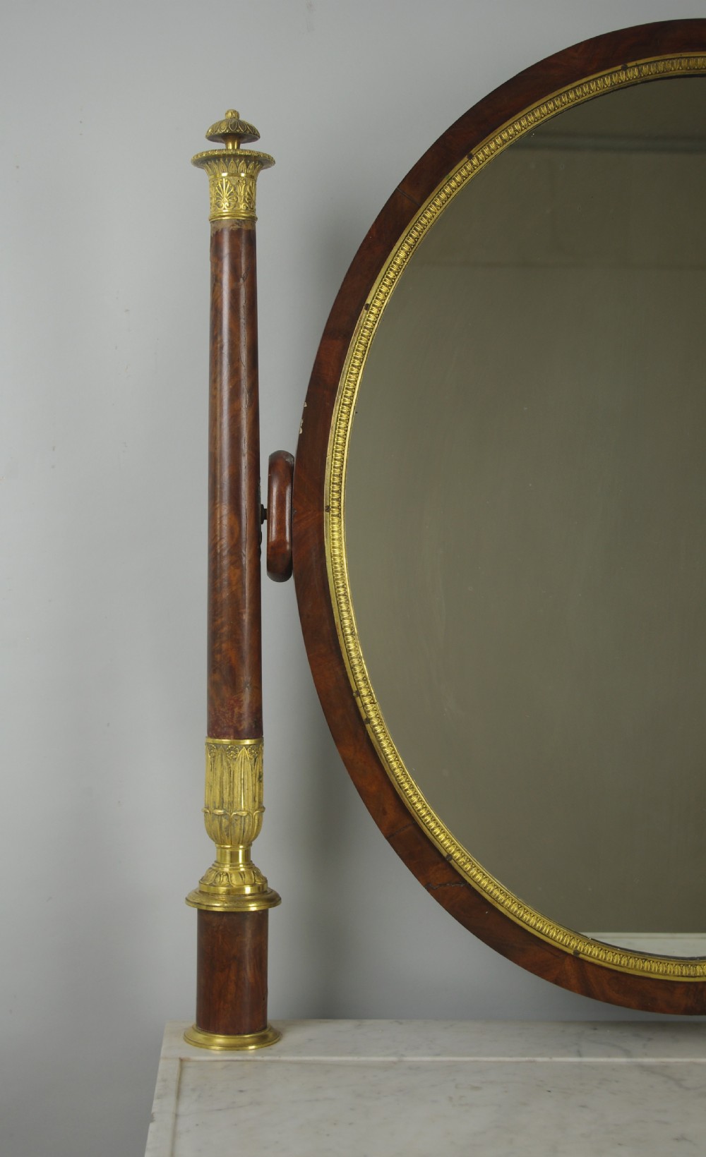 A French Empire mahogany dressing table featuring an oval swivel mirror flanked by gilt-bronze capped columns, set above a marble surface and drawer base with ormolu appliques. View VIII