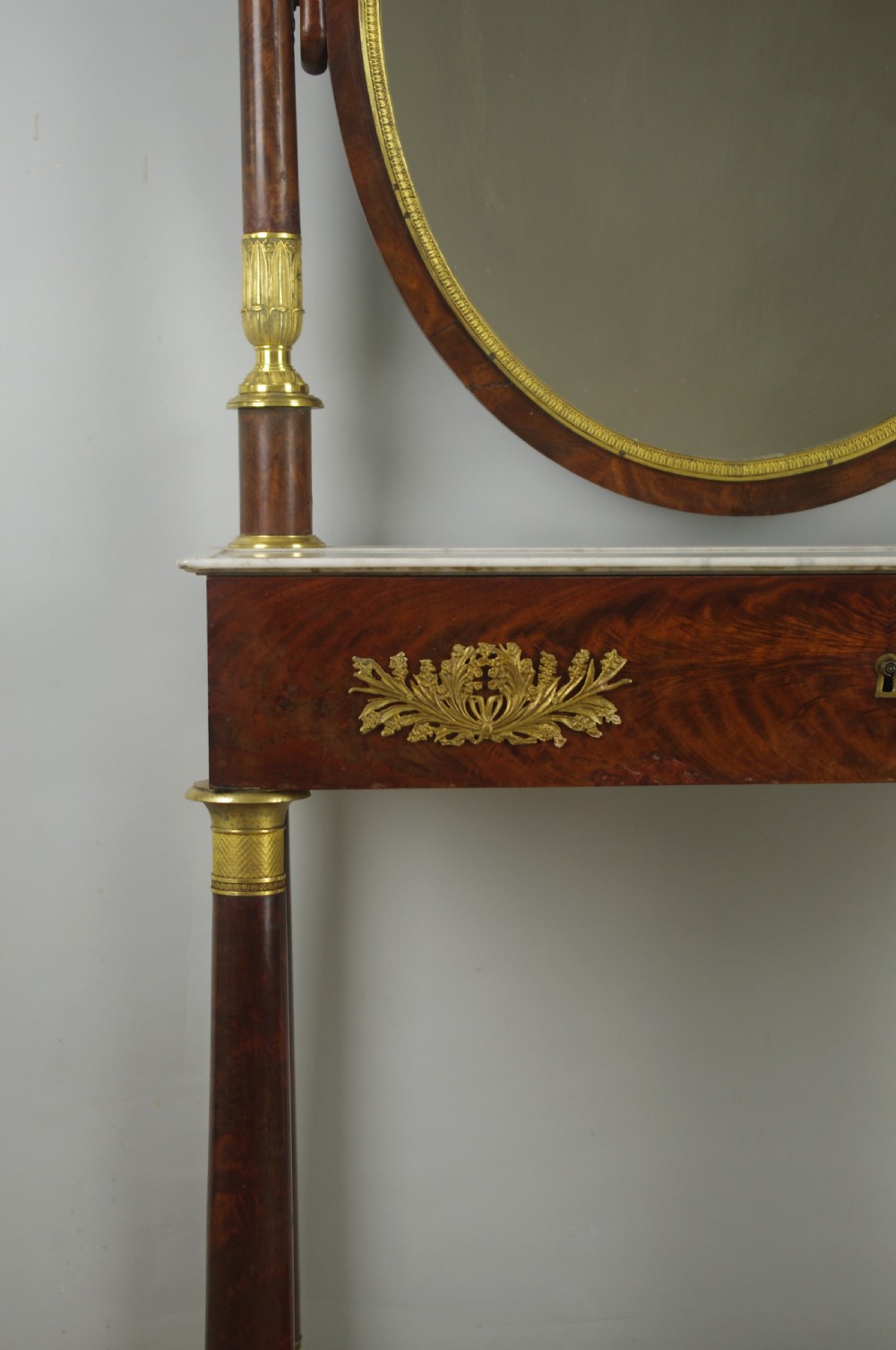 A French Empire mahogany dressing table featuring an oval swivel mirror flanked by gilt-bronze capped columns, set above a marble surface and drawer base with ormolu appliques. View XIV