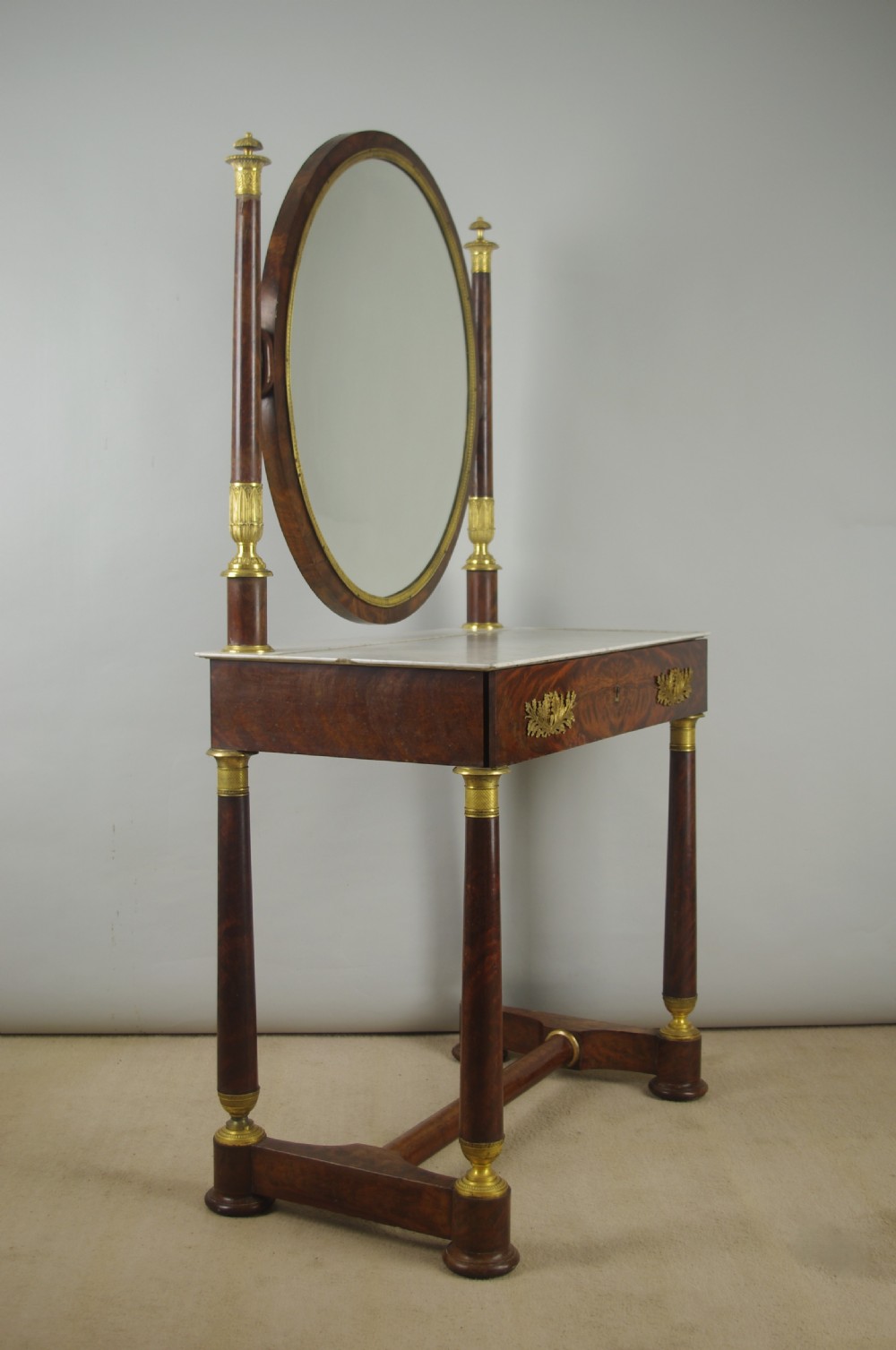 A French Empire mahogany dressing table featuring an oval swivel mirror flanked by gilt-bronze capped columns, set above a marble surface and drawer base with ormolu appliques. View XVIII