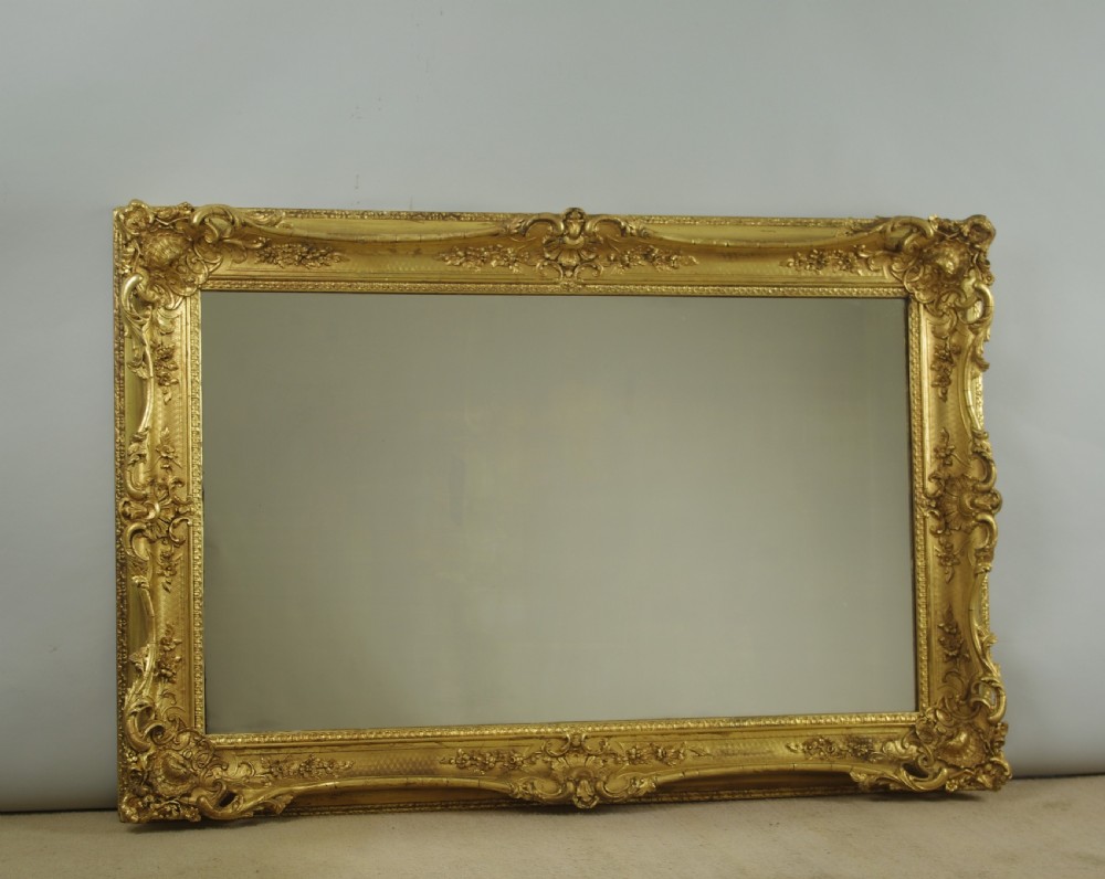 A large rectangular Victorian giltwood wall mirror featuring an ornate swept frame with shell and scroll corner mouldings.