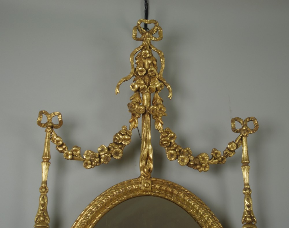 A pair of gilded oval wall mirrors featuring top ribbon bow cresting, hanging floral garlands, and small integrated display shelves. View IV
