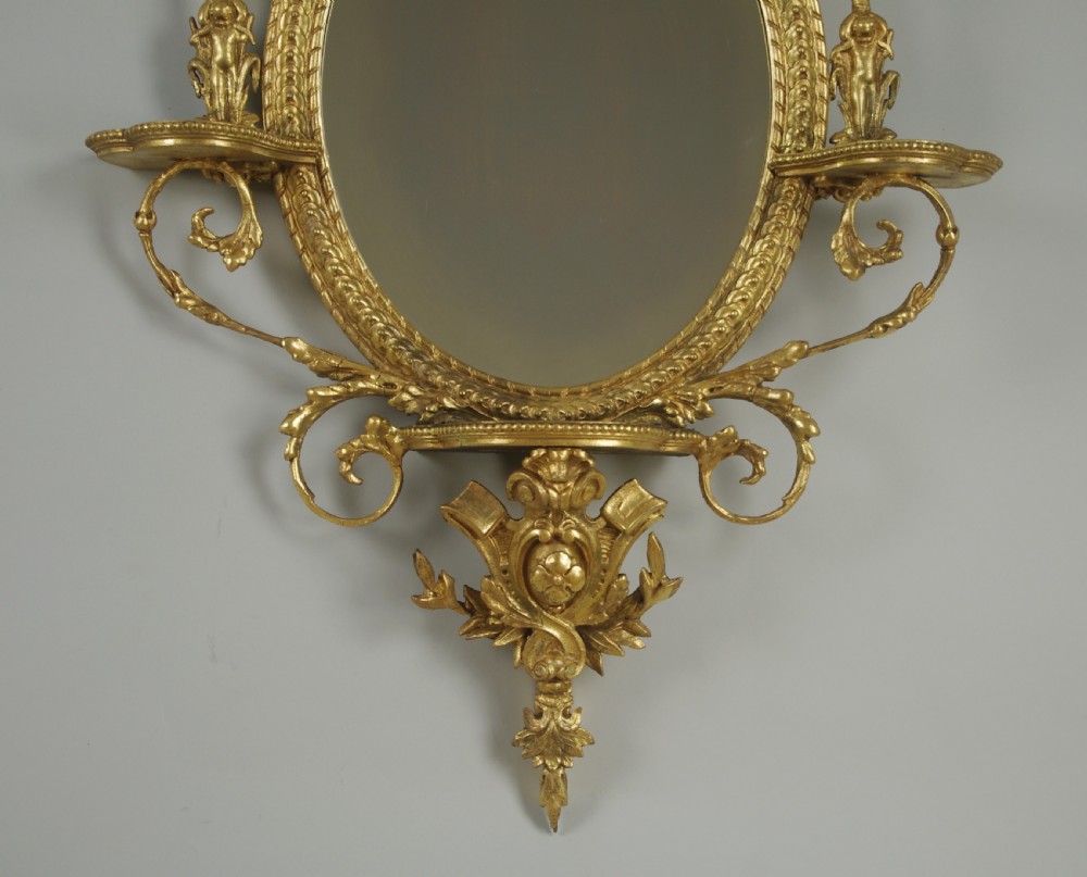 A pair of gilded oval wall mirrors featuring top ribbon bow cresting, hanging floral garlands, and small integrated display shelves. View VII