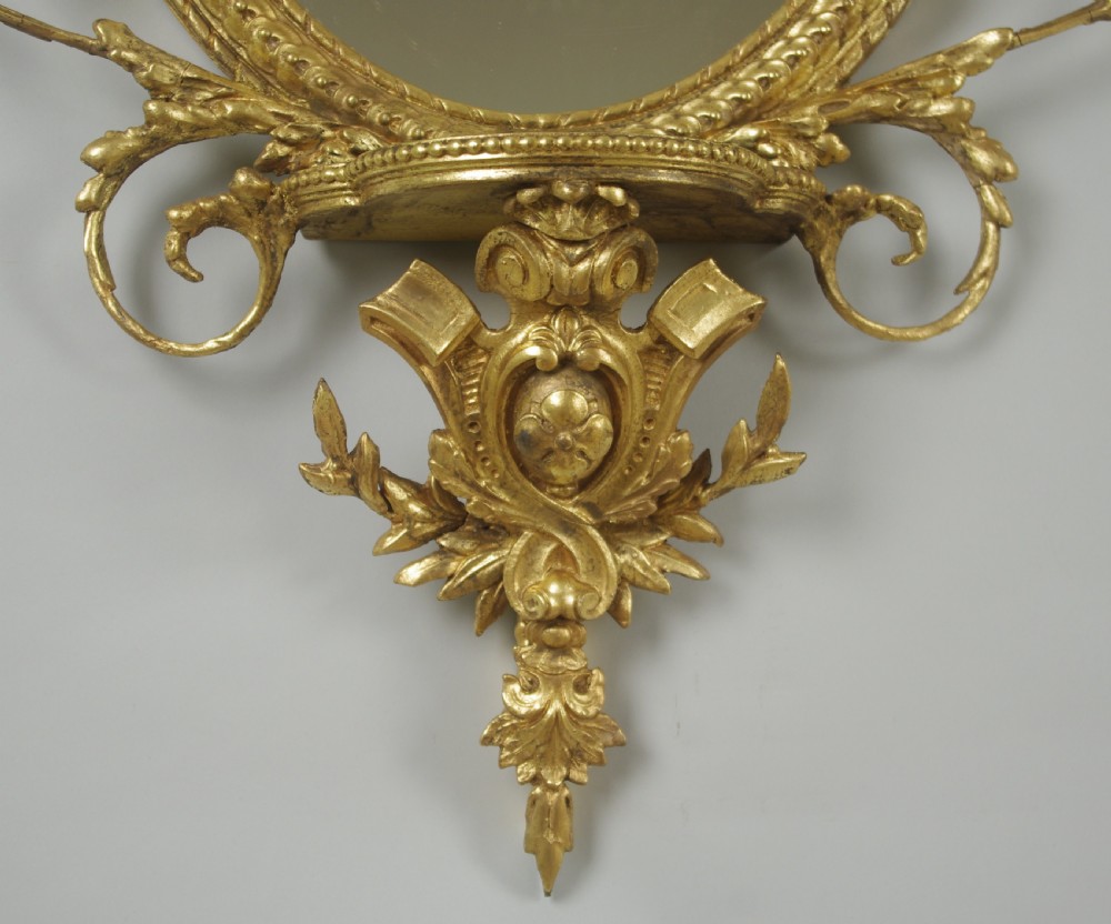 A pair of gilded oval wall mirrors featuring top ribbon bow cresting, hanging floral garlands, and small integrated display shelves. View XI