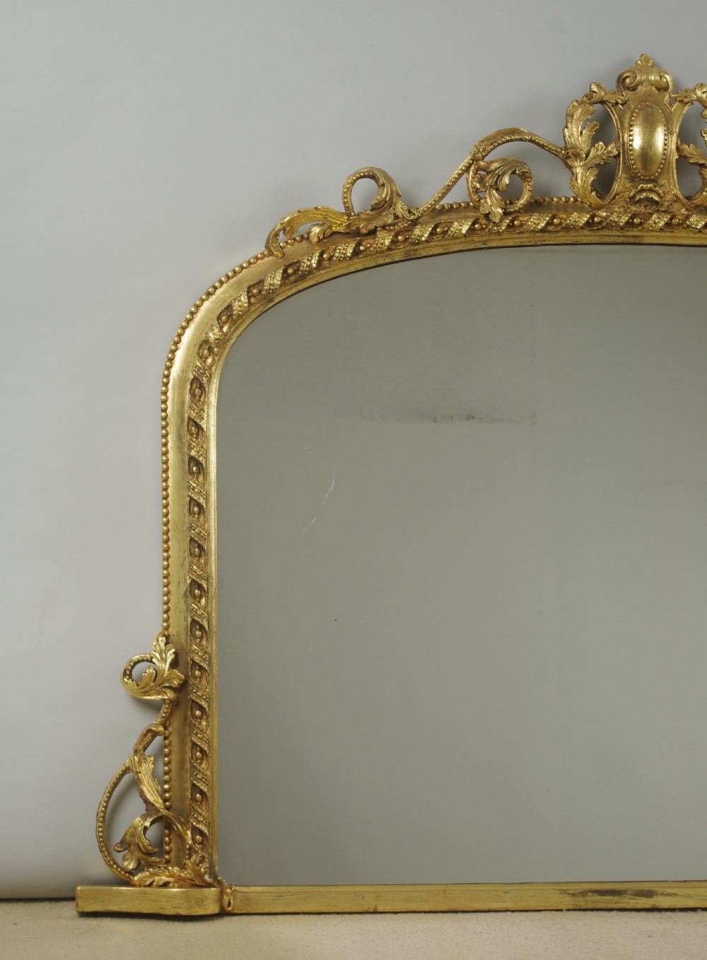 A Victorian giltwood overmantel mirror with an arched frame, central acanthus leaf cresting, twisted rope moulding, and scrolling side brackets. View II