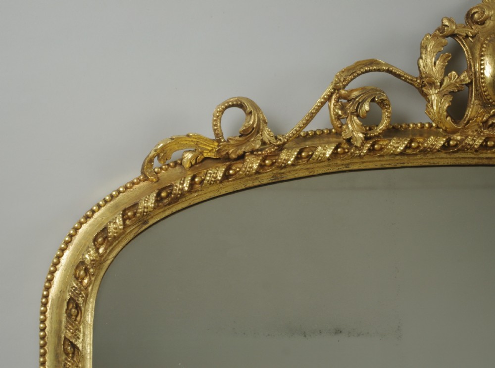 A Victorian giltwood overmantel mirror with an arched frame, central acanthus leaf cresting, twisted rope moulding, and scrolling side brackets. View V