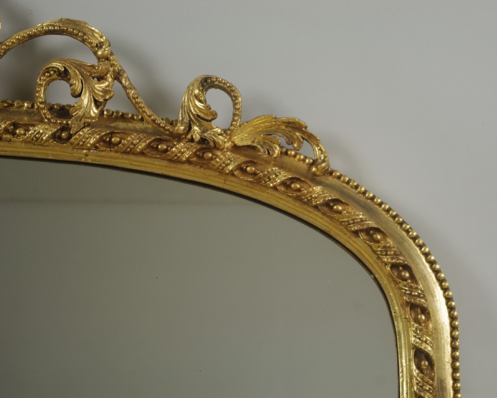 A Victorian giltwood overmantel mirror with an arched frame, central acanthus leaf cresting, twisted rope moulding, and scrolling side brackets. View VI