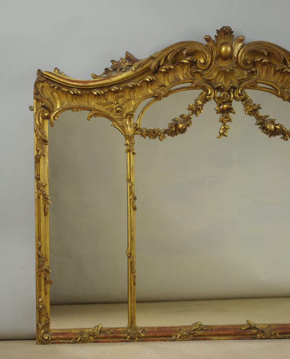 A 19th-century Rococo style giltwood overmantel mirror featuring three mirror plates, carved floral garlands, and a cresting. View II
