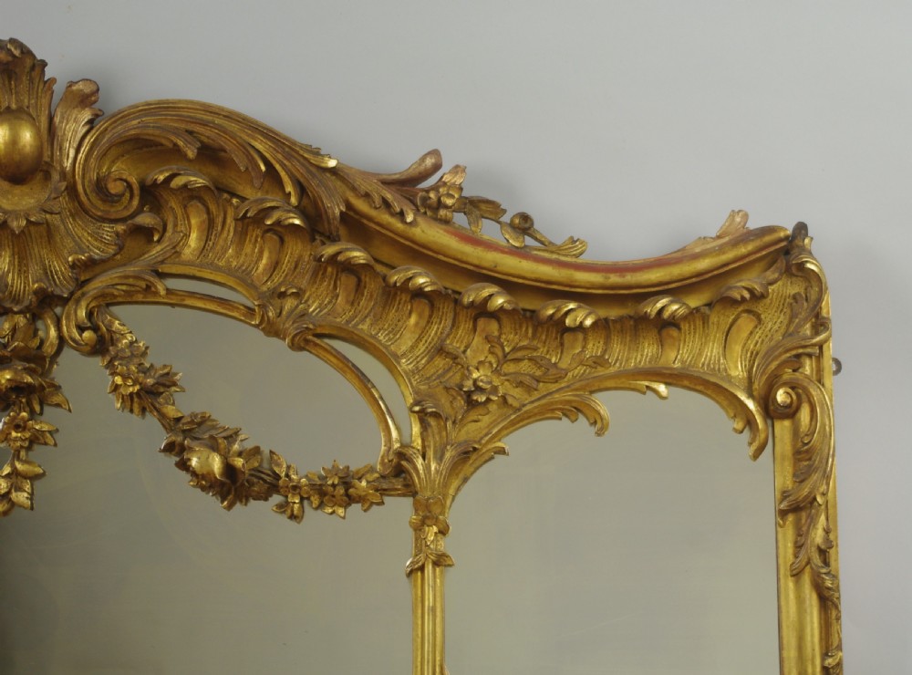 A 19th-century Rococo style giltwood overmantel mirror featuring three mirror plates, carved floral garlands, and a cresting. View V