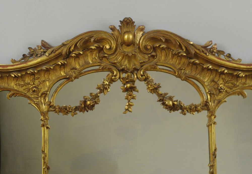 A 19th-century Rococo style giltwood overmantel mirror featuring three mirror plates, carved floral garlands, and a cresting. View VI
