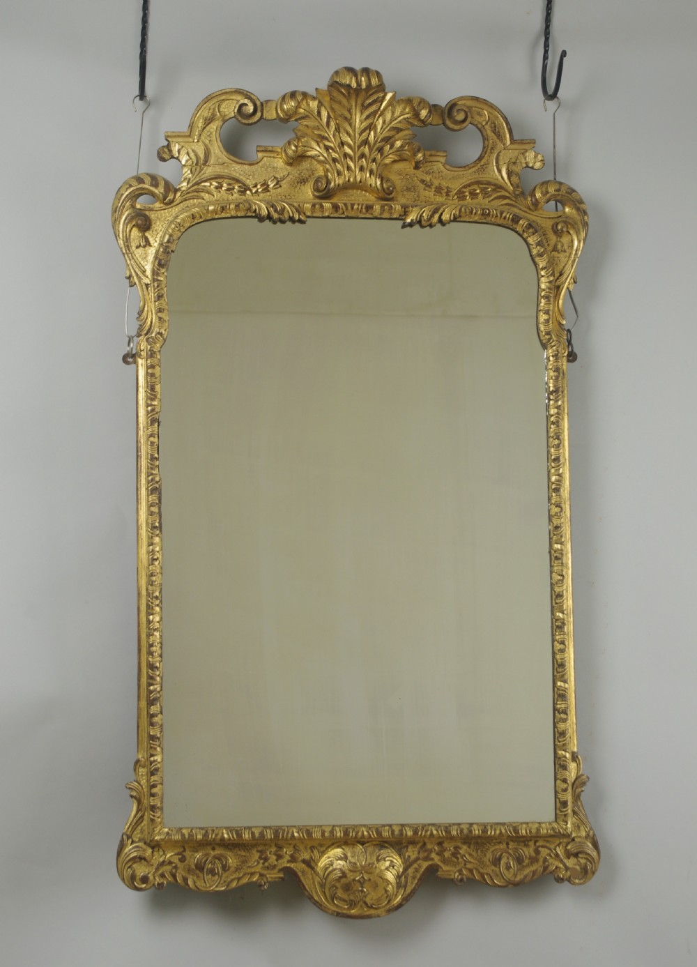 A rectangular 19th-century giltwood wall mirror featuring carved acanthus leaf cresting and scroll details in an aged gold finish.