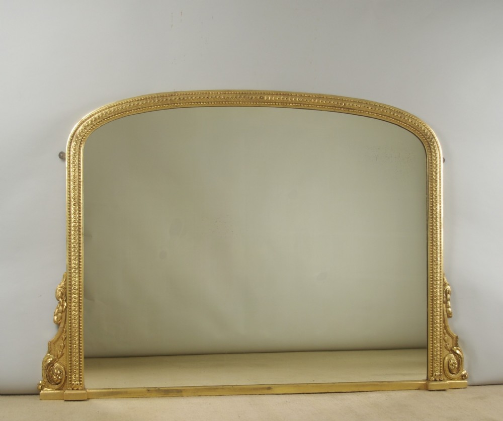 A large Victorian arched overmantel mirror featuring a gilt frame decorated with beaded moulding and scrolled corbels at the base.