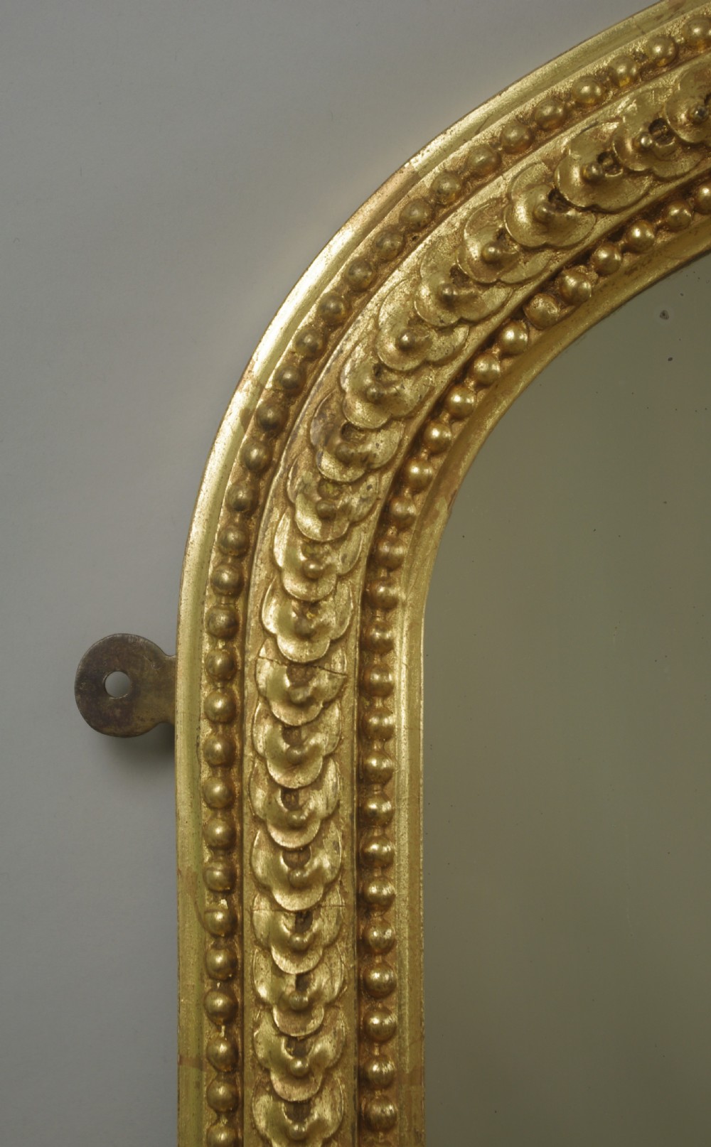 A large Victorian arched overmantel mirror featuring a gilt frame decorated with beaded moulding and scrolled corbels at the base. View VII