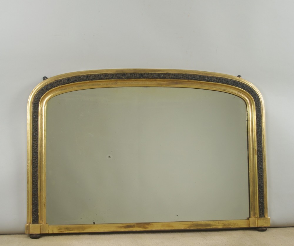 A Victorian arched overmantle mirror featuring a gilt outer frame and an inner carved ebonised moulding band.