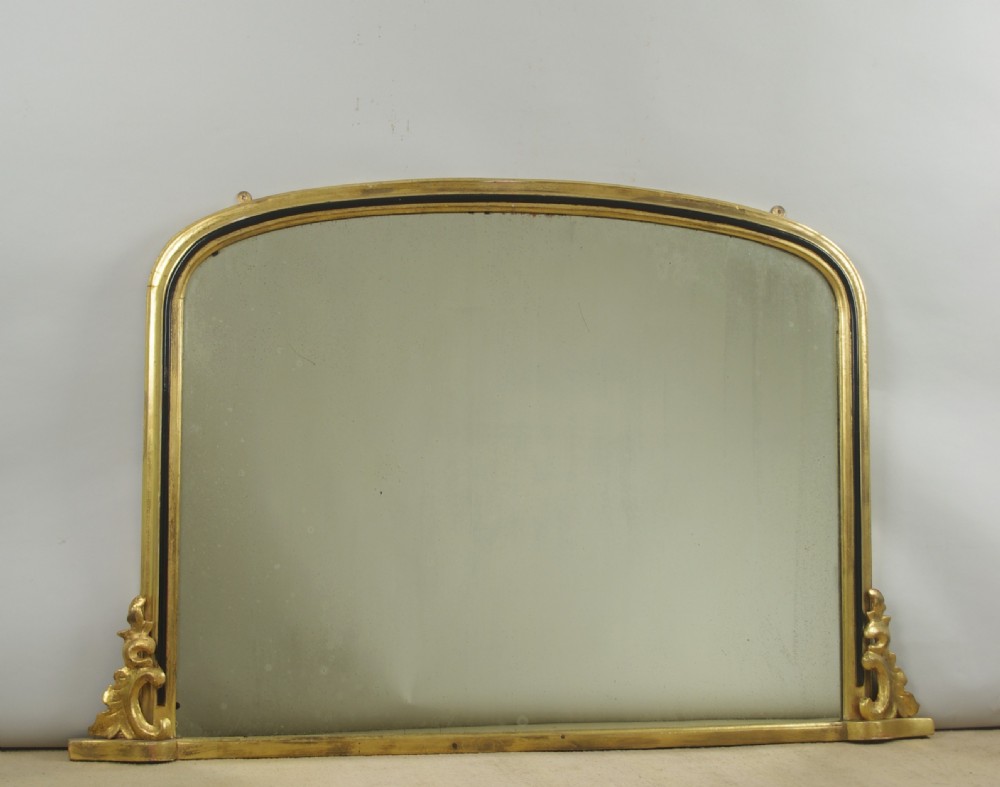 A Victorian arched overmantel mirror featuring a gilded outer frame with an ebonised inner border and carved side scrolls.