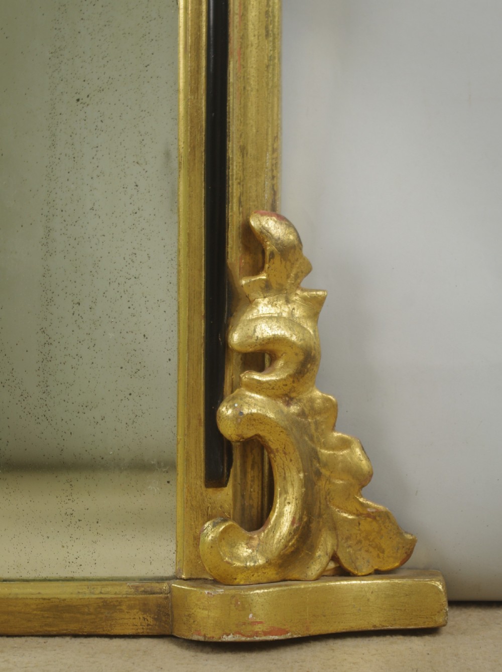 A Victorian arched overmantel mirror featuring a gilded outer frame with an ebonised inner border and carved side scrolls. View VI