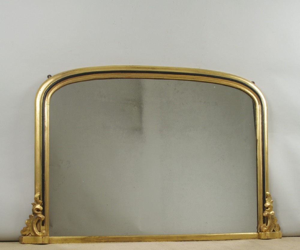 A large Victorian arch top overmantel mirror featuring a gilt frame with an inner ebonised moulding and carved scroll corner feet.