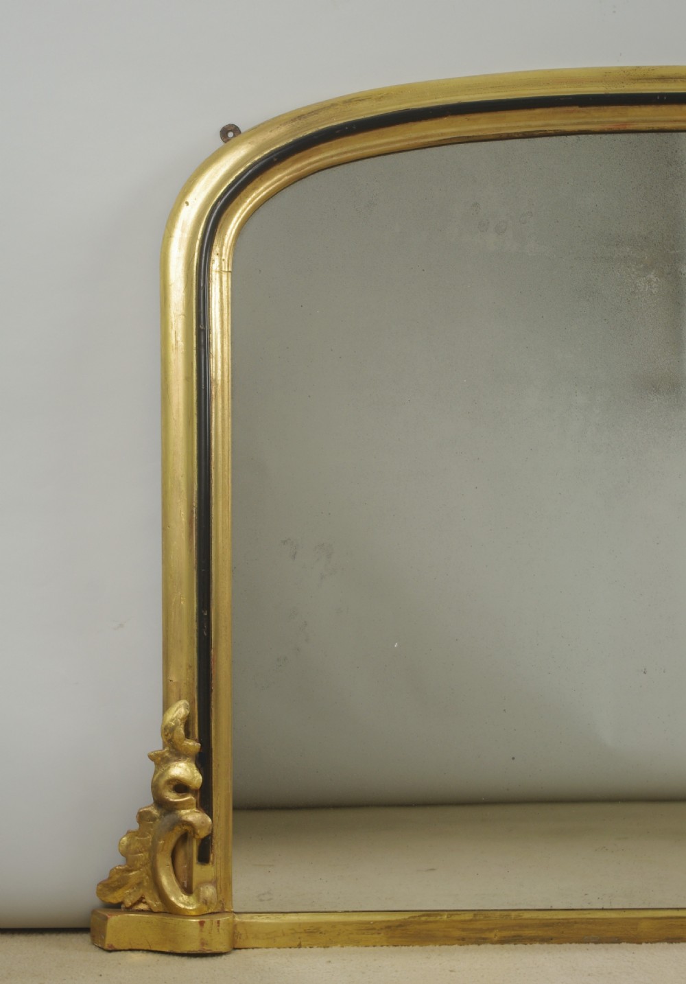 A large Victorian arch top overmantel mirror featuring a gilt frame with an inner ebonised moulding and carved scroll corner feet. View II