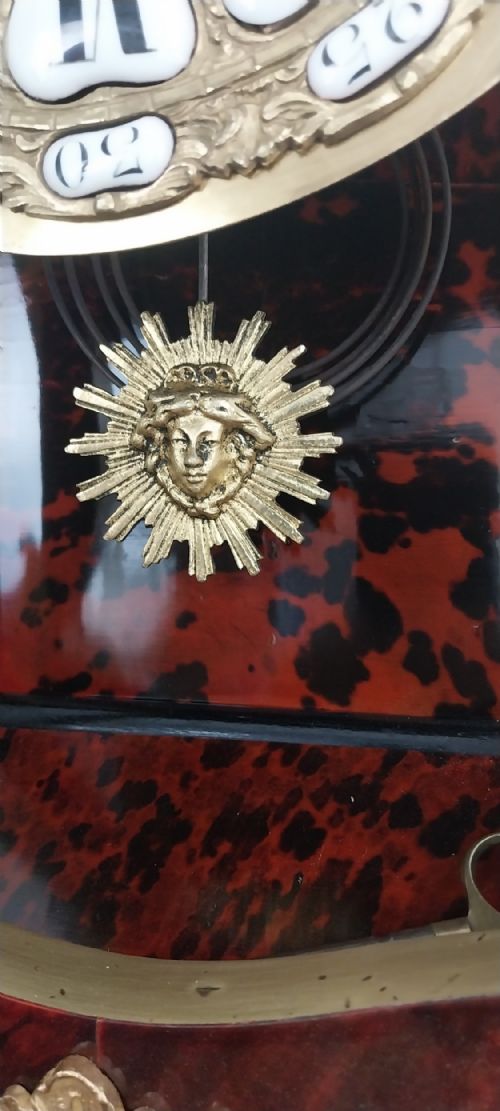 fig 4. An antique French Rococo revival Boulle wall clock featuring a red tortoiseshell case adorned with elaborate gilt bronze mounts, a figure finial, and an enamel cartouche dial on a matching wall bracket.