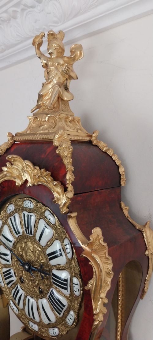 fig 5. An antique French Rococo revival Boulle wall clock featuring a red tortoiseshell case adorned with elaborate gilt bronze mounts, a figure finial, and an enamel cartouche dial on a matching wall bracket.