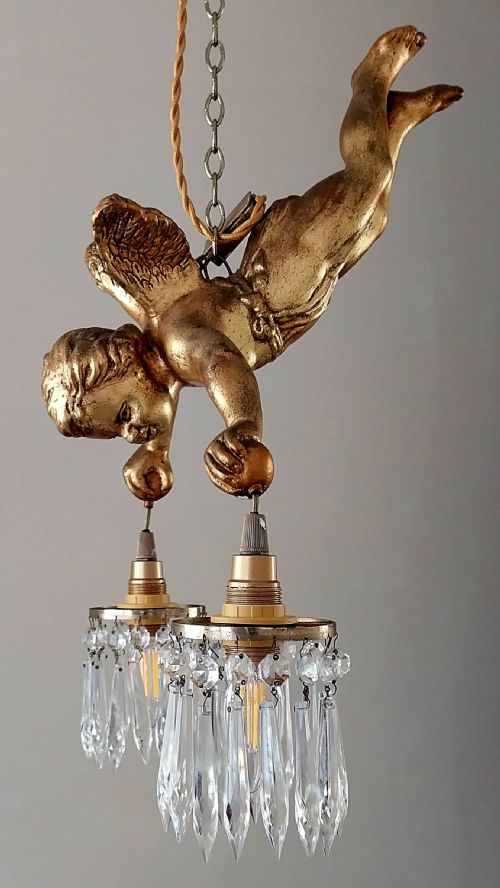 fig 1. An antique gilded winged cherub hanging ceiling light fixture suspended by a chain, holding two light sockets dressed with crystal droplets.
