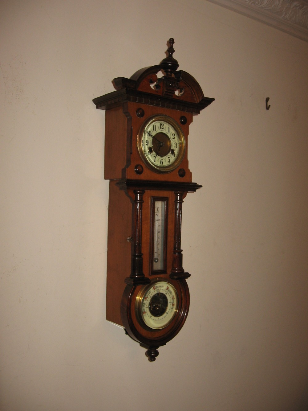 A late Victorian carved wooden wall clock featuring an upper clock face, a central thermometer, and a lower barometer dial.