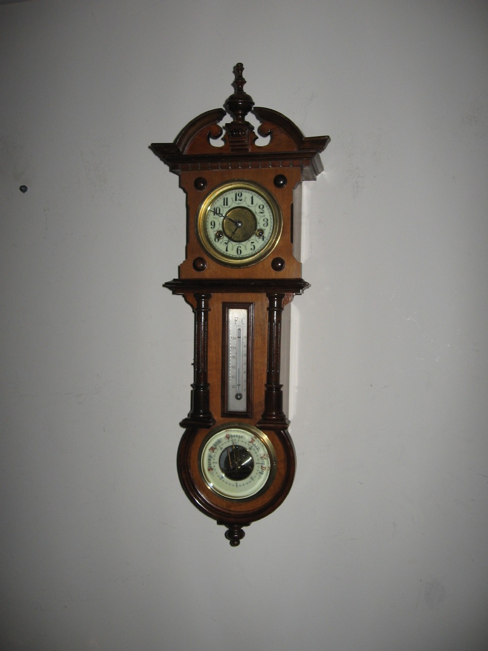 A late Victorian carved wooden wall clock featuring an upper clock face, a central thermometer, and a lower barometer dial. View II