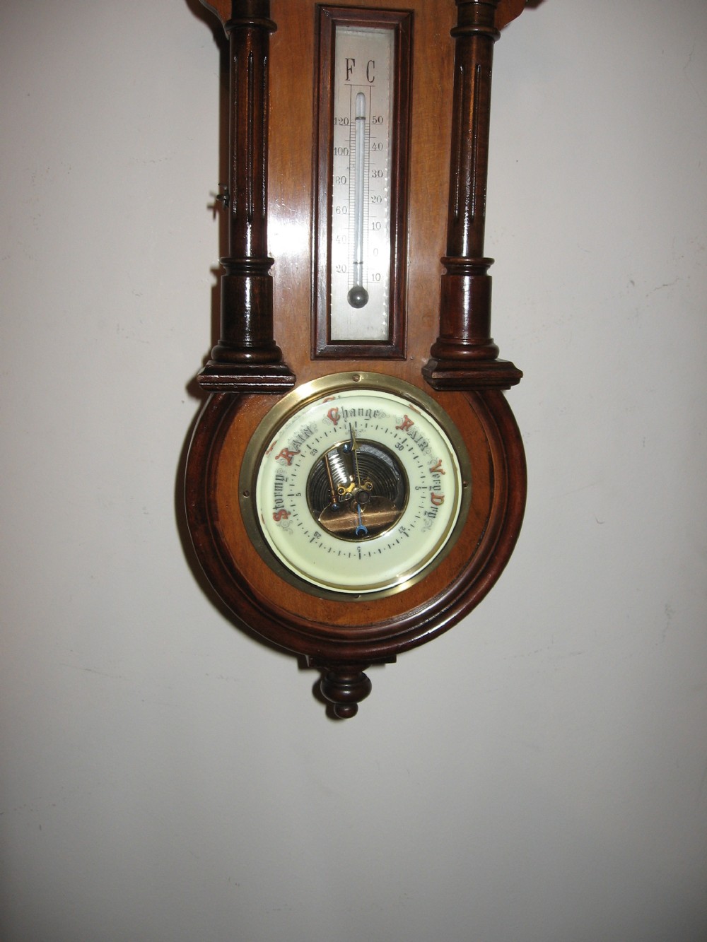 A late Victorian carved wooden wall clock featuring an upper clock face, a central thermometer, and a lower barometer dial. View VI