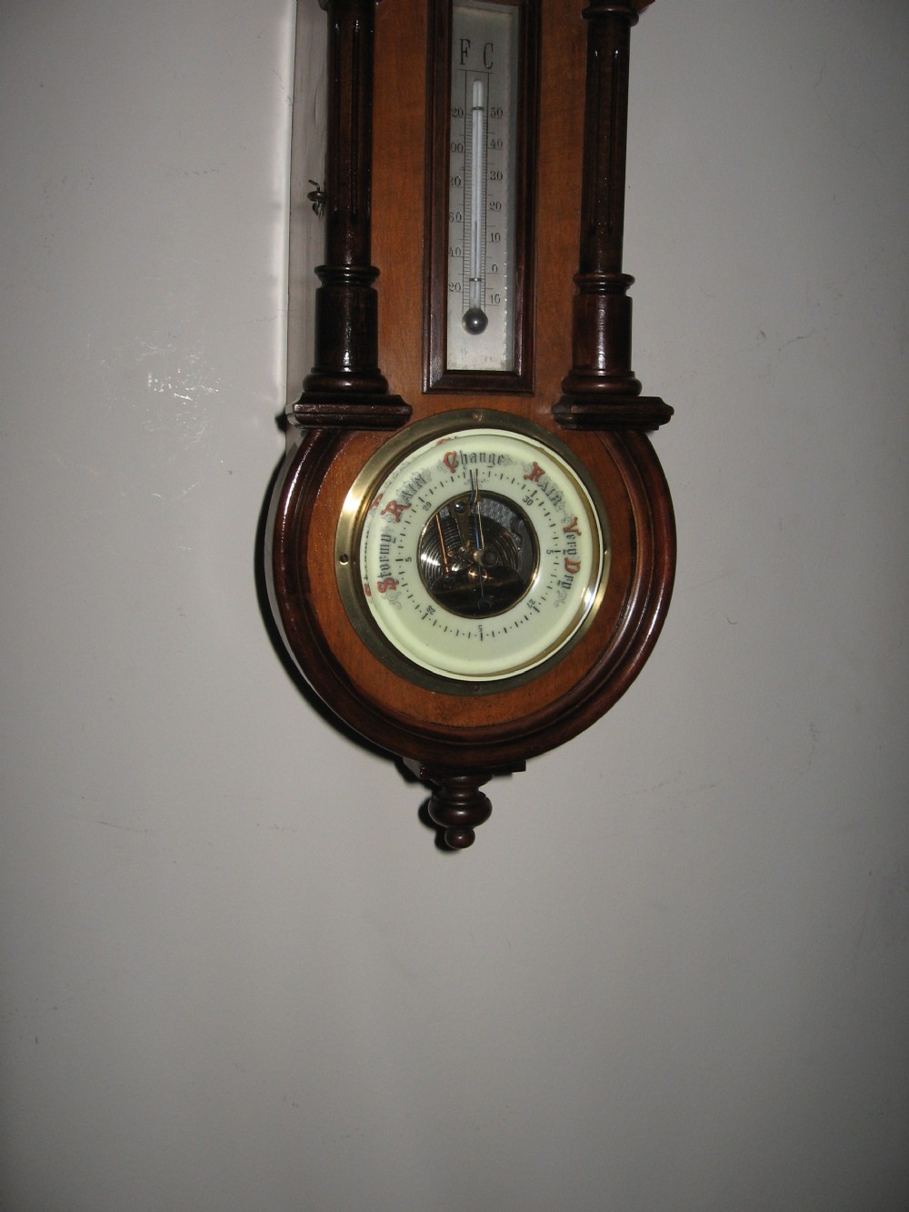 A late Victorian carved wooden wall clock featuring an upper clock face, a central thermometer, and a lower barometer dial. View VII