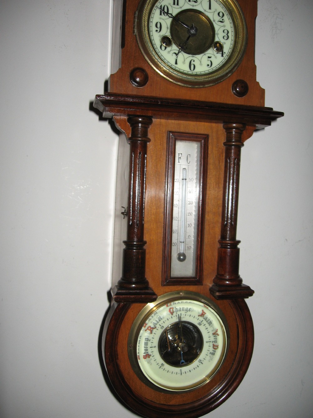 A late Victorian carved wooden wall clock featuring an upper clock face, a central thermometer, and a lower barometer dial. View VIII