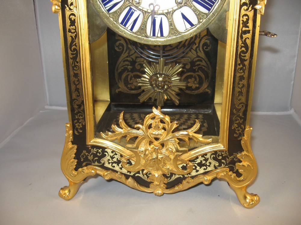 An ornate French Boulle mantel clock decorated with brass marquetry, gilt bronze mounts, a winged cherub finial, and white enamel Roman numeral cartouches. View V