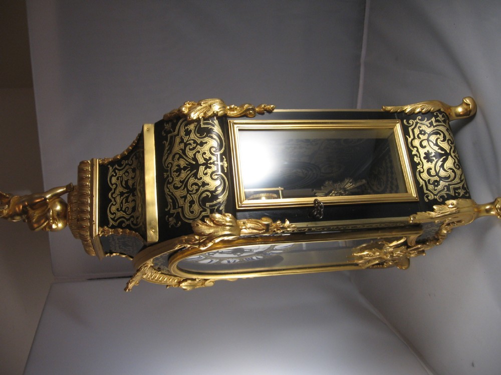 An ornate French Boulle mantel clock decorated with brass marquetry, gilt bronze mounts, a winged cherub finial, and white enamel Roman numeral cartouches. View VI