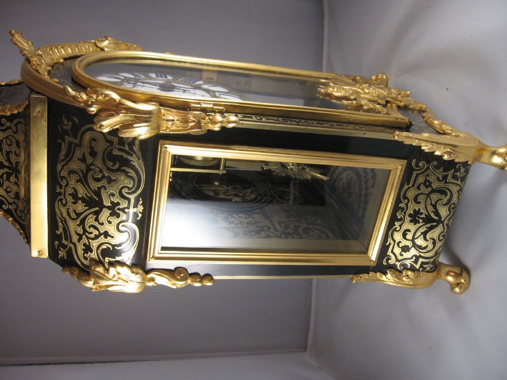 An ornate French Boulle mantel clock decorated with brass marquetry, gilt bronze mounts, a winged cherub finial, and white enamel Roman numeral cartouches. View IX