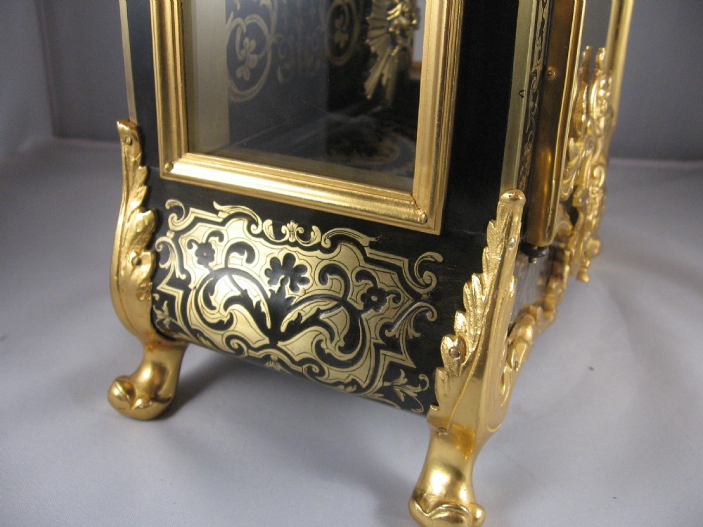 An ornate French Boulle mantel clock decorated with brass marquetry, gilt bronze mounts, a winged cherub finial, and white enamel Roman numeral cartouches. View X