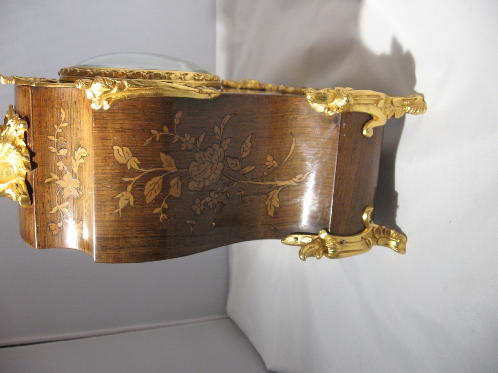 A nineteenth-century French Rococo style mantel clock crafted from dark rosewood with floral marquetry inlay, ornate gilt-bronze mounts, and a white enamel dial. View II