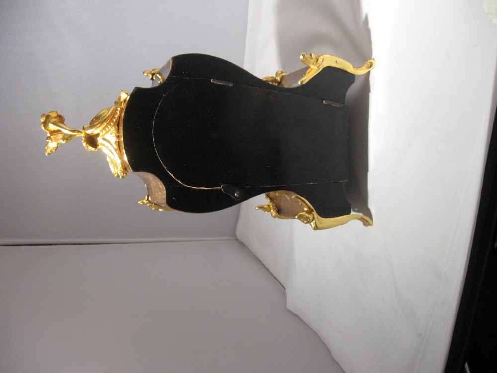 A nineteenth-century French Rococo style mantel clock crafted from dark rosewood with floral marquetry inlay, ornate gilt-bronze mounts, and a white enamel dial. View VI