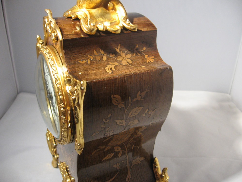 A nineteenth-century French Rococo style mantel clock crafted from dark rosewood with floral marquetry inlay, ornate gilt-bronze mounts, and a white enamel dial. View VII
