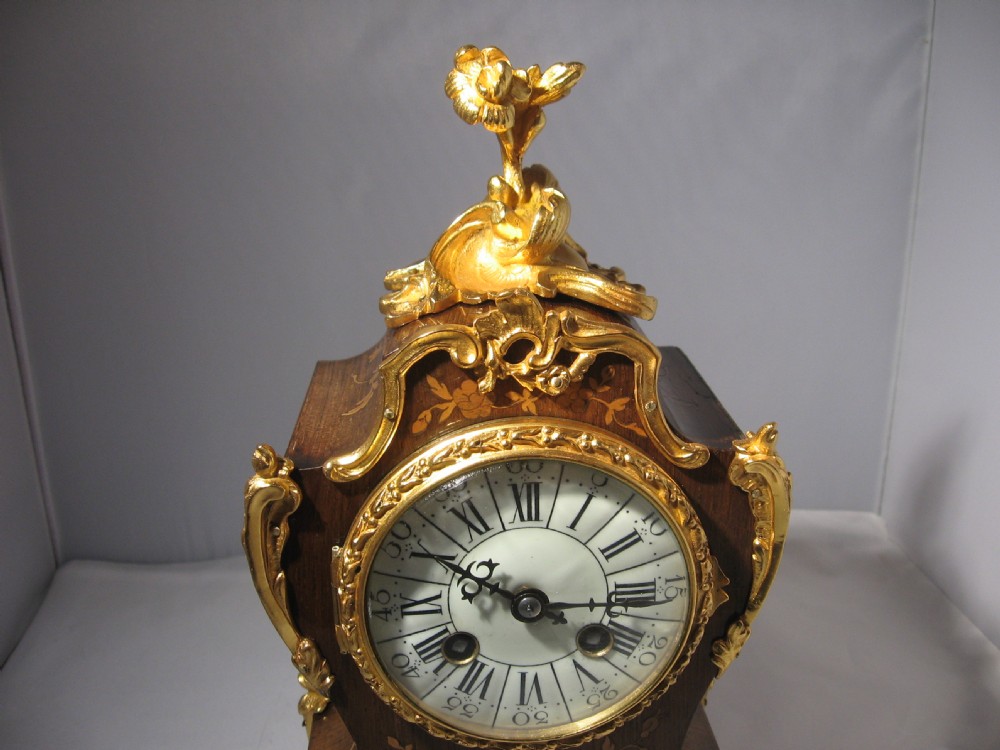 A nineteenth-century French Rococo style mantel clock crafted from dark rosewood with floral marquetry inlay, ornate gilt-bronze mounts, and a white enamel dial. View XI