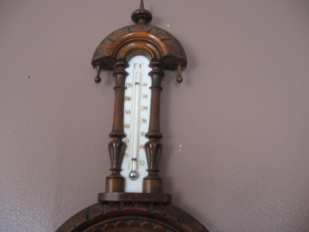 A carved dark walnut wall barometer featuring a vertical thermometer at the top and a circular aneroid pressure dial at the base. View III