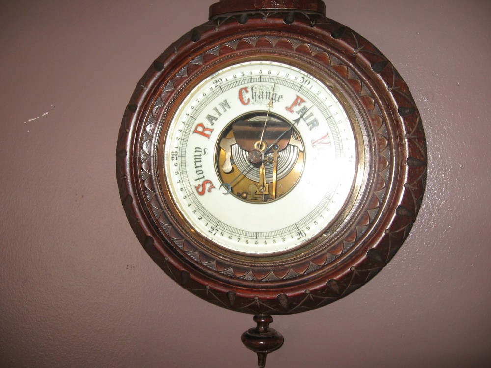A carved dark walnut wall barometer featuring a vertical thermometer at the top and a circular aneroid pressure dial at the base. View IV
