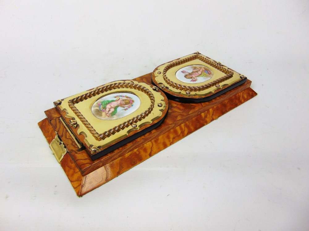An expanding wooden book slide featuring golden burr wood veneer, folding arched ends, and a gilt brass front plate framing an oval painted porcelain cherub medallion. View II